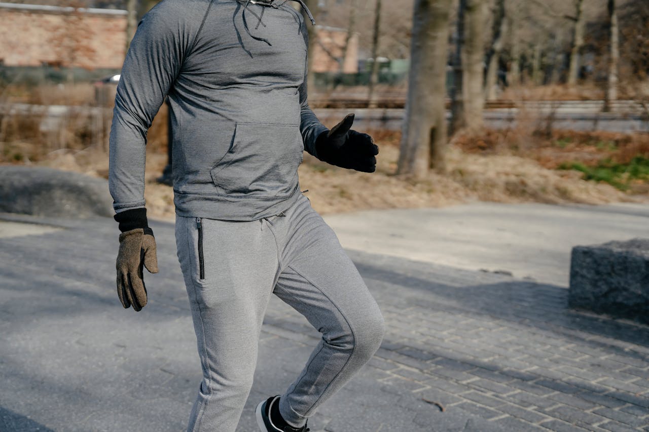 Crop anonymous male in sportswear and gloves jumping on one leg while warming up before workout training in city park